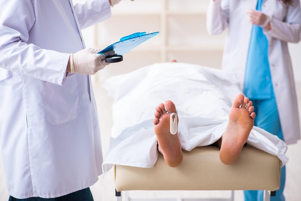 Police coroner examining dead body corpse in morgue.