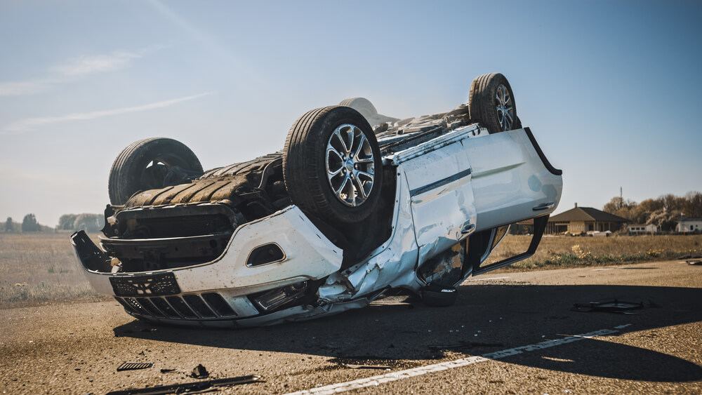 Rollover smoking and burning vehicle lying on its roof in the middle of the road after collision.